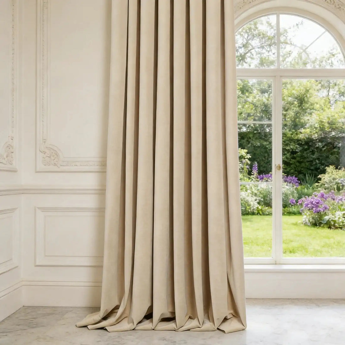 Side view showing the elegant drape and smooth texture of a single beige Adrian cashmere blackout curtain panel hanging next to an arched window and detailed wall paneling.