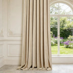 Side view showing the elegant drape and smooth texture of a single beige Adrian cashmere blackout curtain panel hanging next to an arched window and detailed wall paneling.