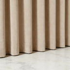 Low-angle close-up detail of the neat bottom hem of beige Adrian extra long and wide cashmere blackout curtains resting on a polished marble floor.