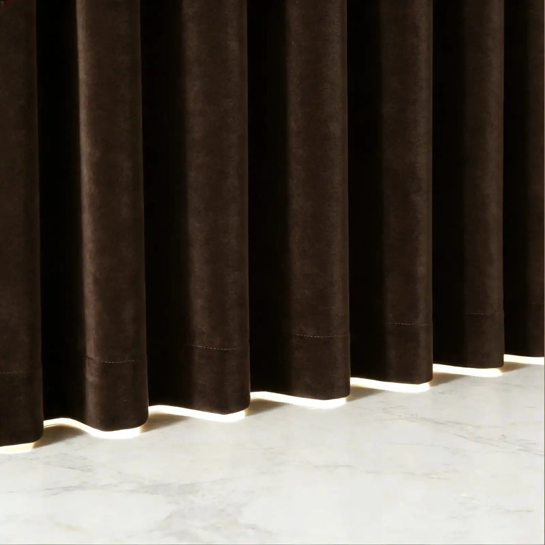 A crisp, tight shot highlighting the uniform pleats and structured vertical folds of the brown curtain fabric next to a wooden table corner and a subtle green branch.