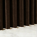 A crisp, tight shot highlighting the uniform pleats and structured vertical folds of the brown curtain fabric next to a wooden table corner and a subtle green branch.
