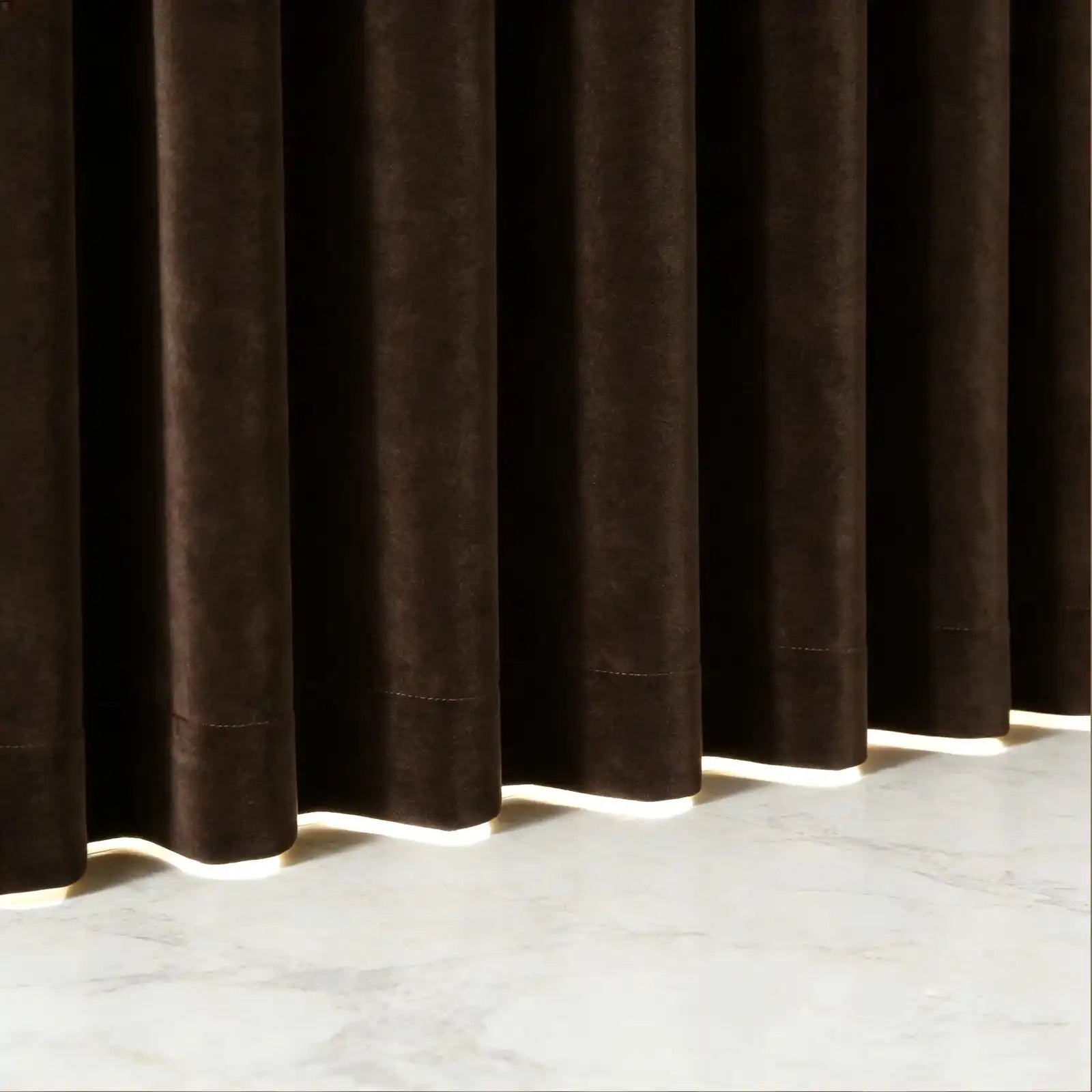 A crisp, tight shot highlighting the uniform pleats and structured vertical folds of the brown curtain fabric next to a wooden table corner and a subtle green branch.
