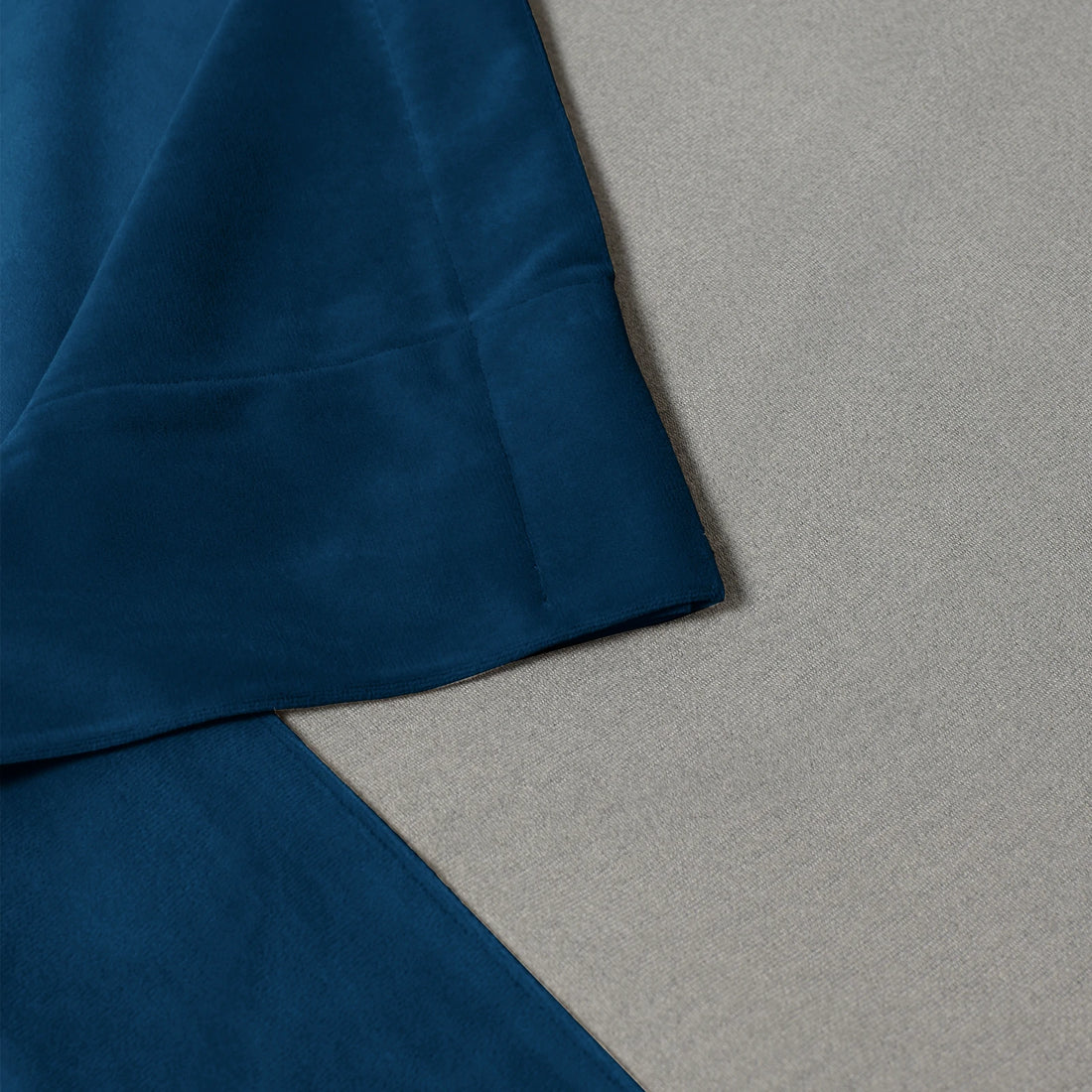 A close-up structural shot detailing the neat, professional stitching on the bottom corner hem of the deep sea blue curtain fabric resting flat against a light gray textured surface.