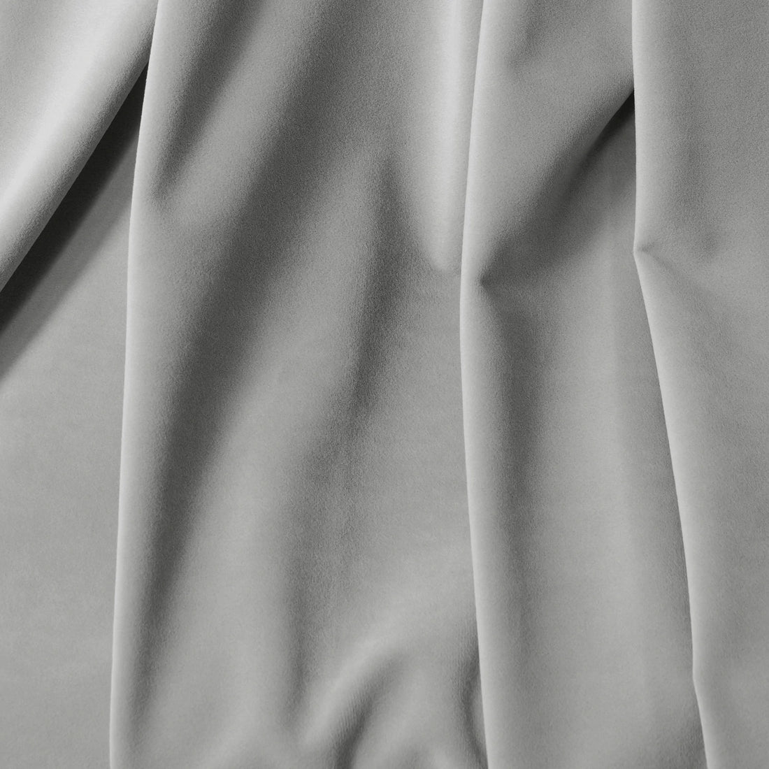 A detailed close-up capturing the graceful vertical drapes, soft texture, and subtle shadows of the light gray curtain material.
