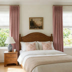 A symmetrical, full-length front view of a classic bedroom setup, where a wooden headboard is flanked perfectly by a pair of elegant pink curtains.