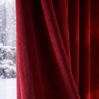 A detailed view of the rich ruby red curtain fabric draped gracefully next to a window pane showcasing softly falling snow outside.