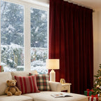 An angled perspective highlighting a single ruby red curtain panel hanging gracefully beside a cream-colored couch and a warm, glowing table lamp.