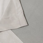 A structural close-up shot detailing the neat, professional corner stitching and hem of the off-white curtain fabric resting flat against a light gray textured surface.