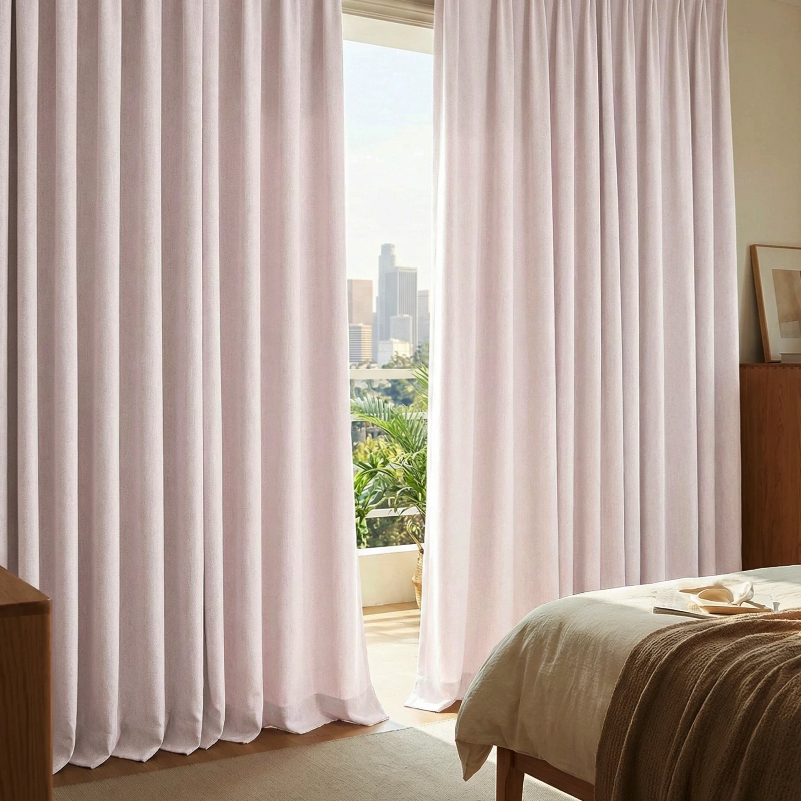 Light pink Alex blackout curtains framing a sunny bedroom balcony and city view