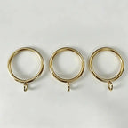 Close-up of gold steel curtain rings with small attachment loops, ideal for window treatment accessories and drapery hanging