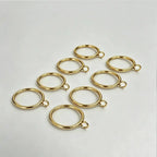 Multiple gold-colored curtain rings with clips arranged on a white surface, designed for easy curtain installation and decoration