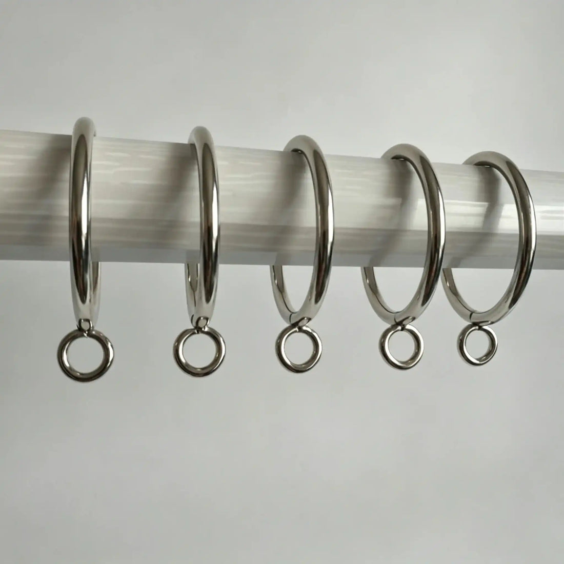 Stainless steel curtain rings with hooks arranged on a white surface, shiny and durable, ideal for window treatments, SKU: AGPC70-1