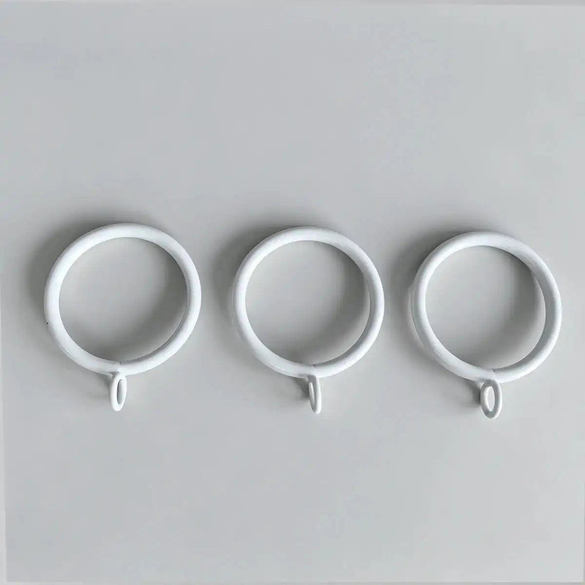 Close-up of white steel curtain rings with loops, arranged on a flat surface, used for fixing curtain spacers, SKU: AGPC70-1