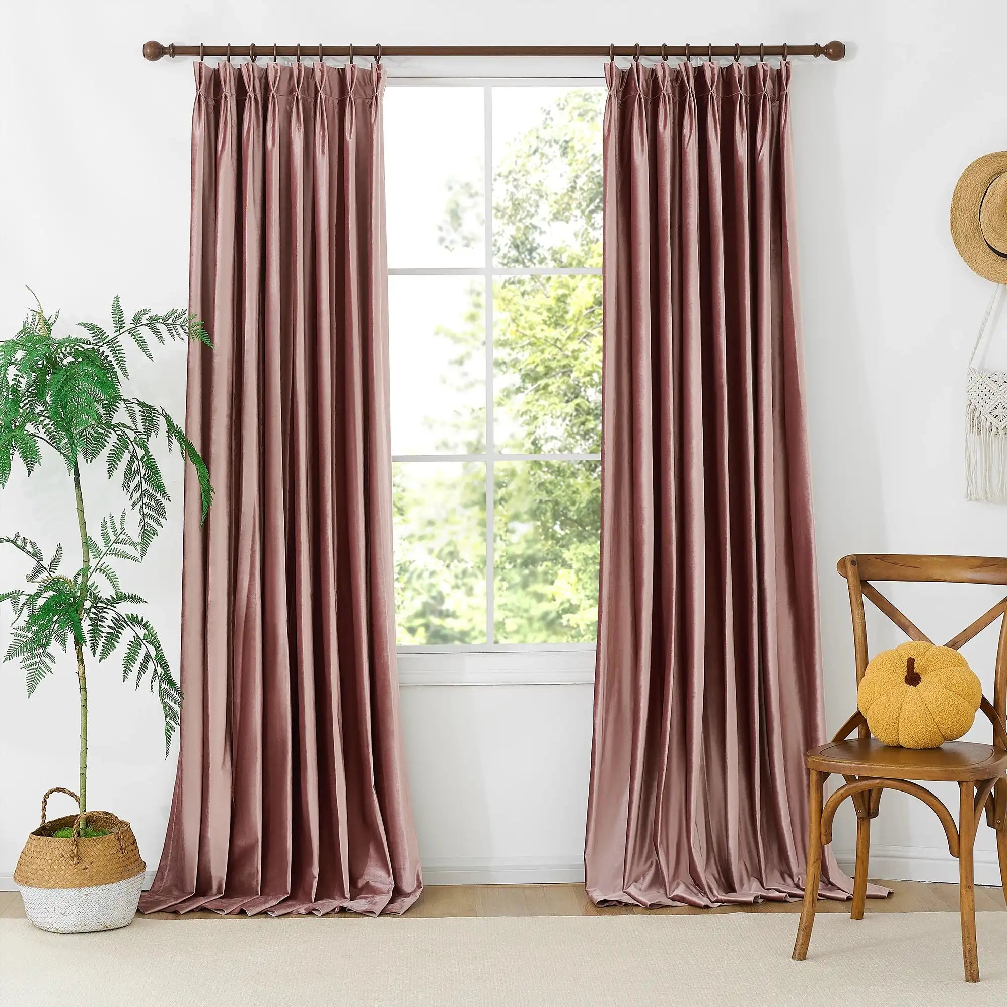 Pink velvet curtains hanging in front of a large window with greenery outside, decorated with a small yellow pouf and a cozy window seat