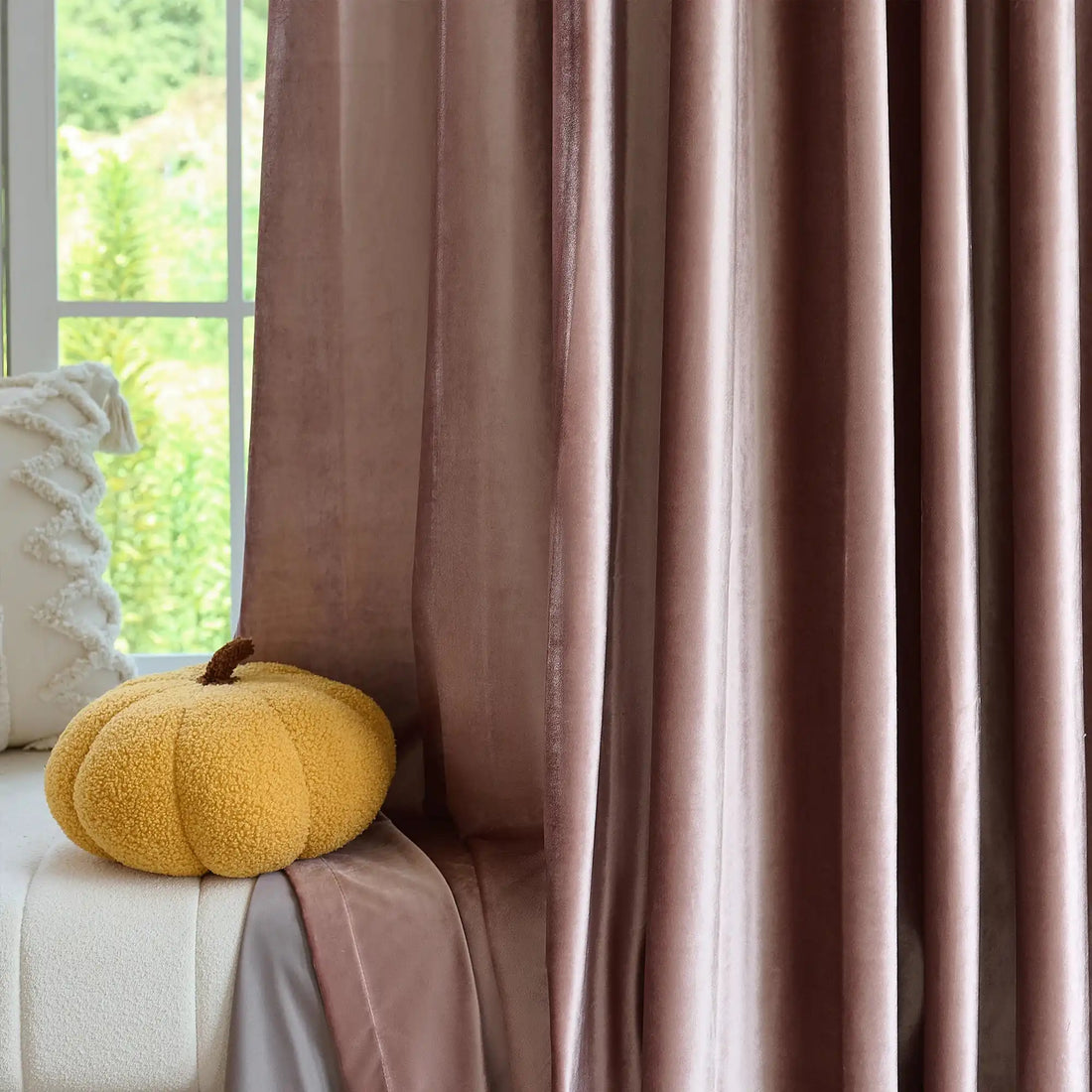 Pink velvet curtains with a soft sheen hanging in front of a window with greenery outside, elegant home decor