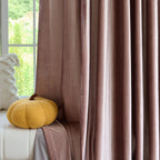 Pink velvet curtains with a soft sheen hanging in front of a window with greenery outside, elegant home decor