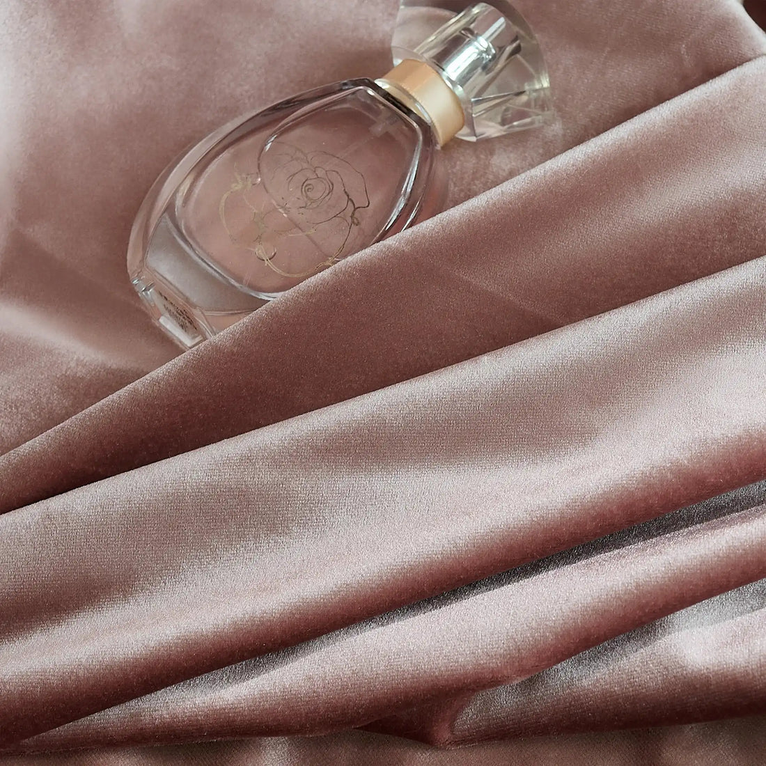 Pink velvet curtains with a smooth, shiny surface, draped in front of a window with natural light and greenery outside