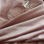 Pink velvet curtains with a smooth, shiny surface, draped in front of a window with natural light and greenery outside