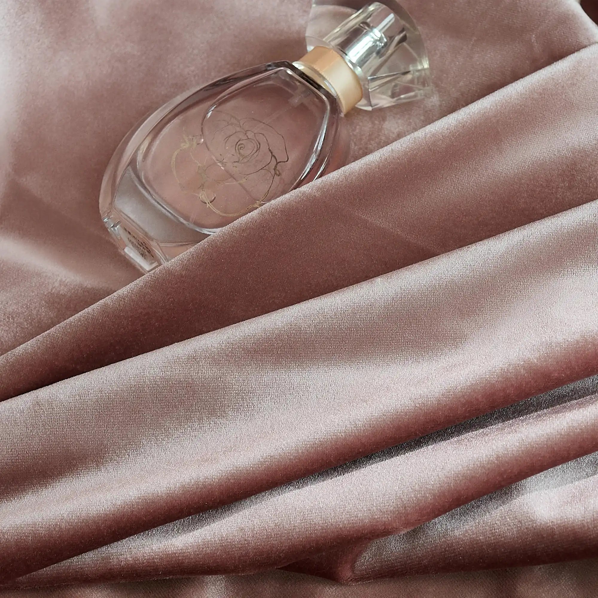 Pink velvet curtains with a smooth, shiny surface, draped in front of a window with natural light and greenery outside