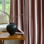Close-up of pink velvet drapes with a luxurious texture, hanging beside a window with lush outdoor scenery