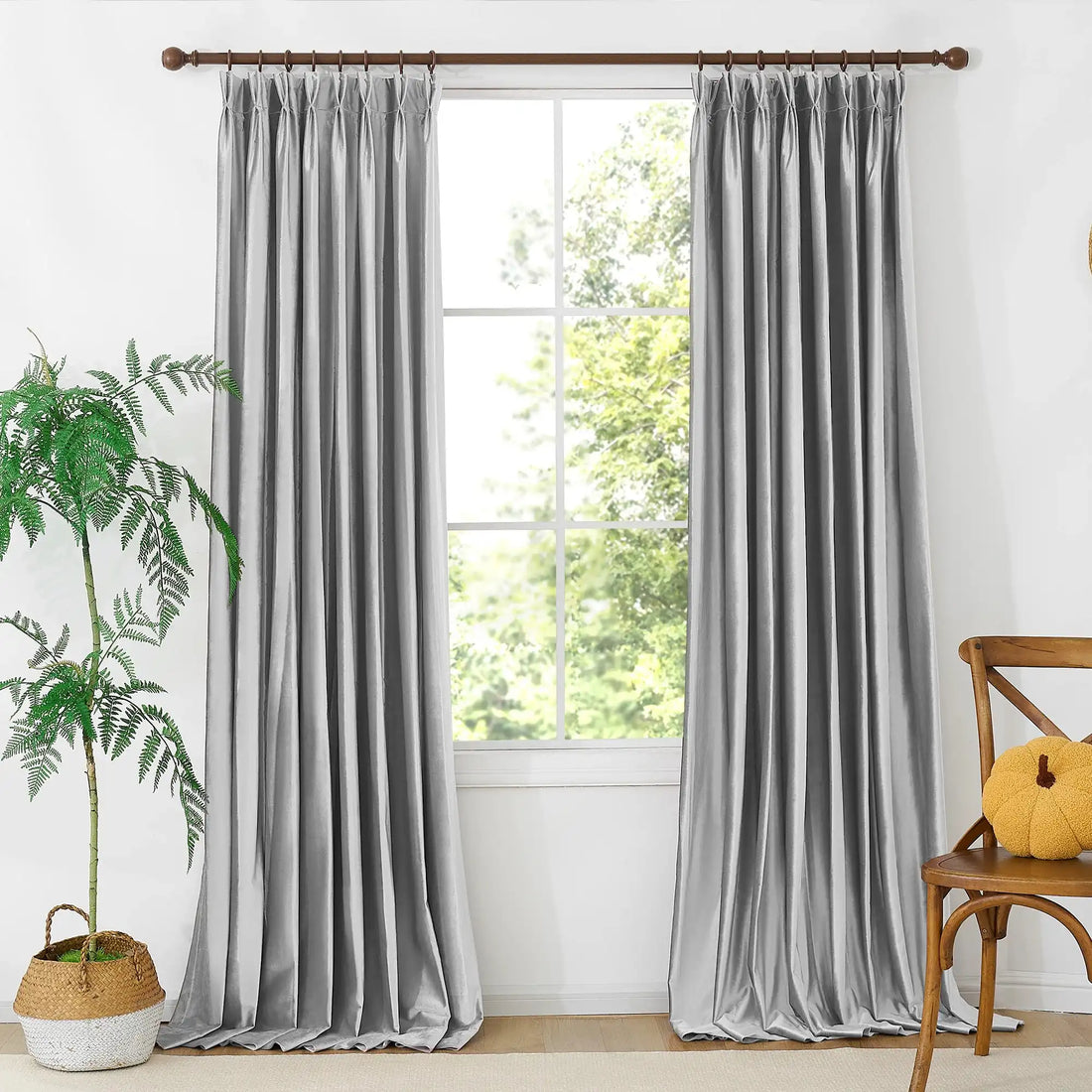 Close-up of gray velvet curtains on a wooden curtain rod, with natural light filtering through, in a bright room with white walls.