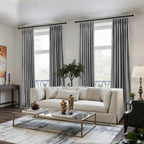 Modern living room featuring gray velvet curtains, a white sofa, a coffee table with decorative vases, and a large window with greenery outside.