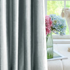 Luxurious gray velvet drapes with a subtle sheen, hanging on a black rod, in a stylish living space with decorative vases and flowers.