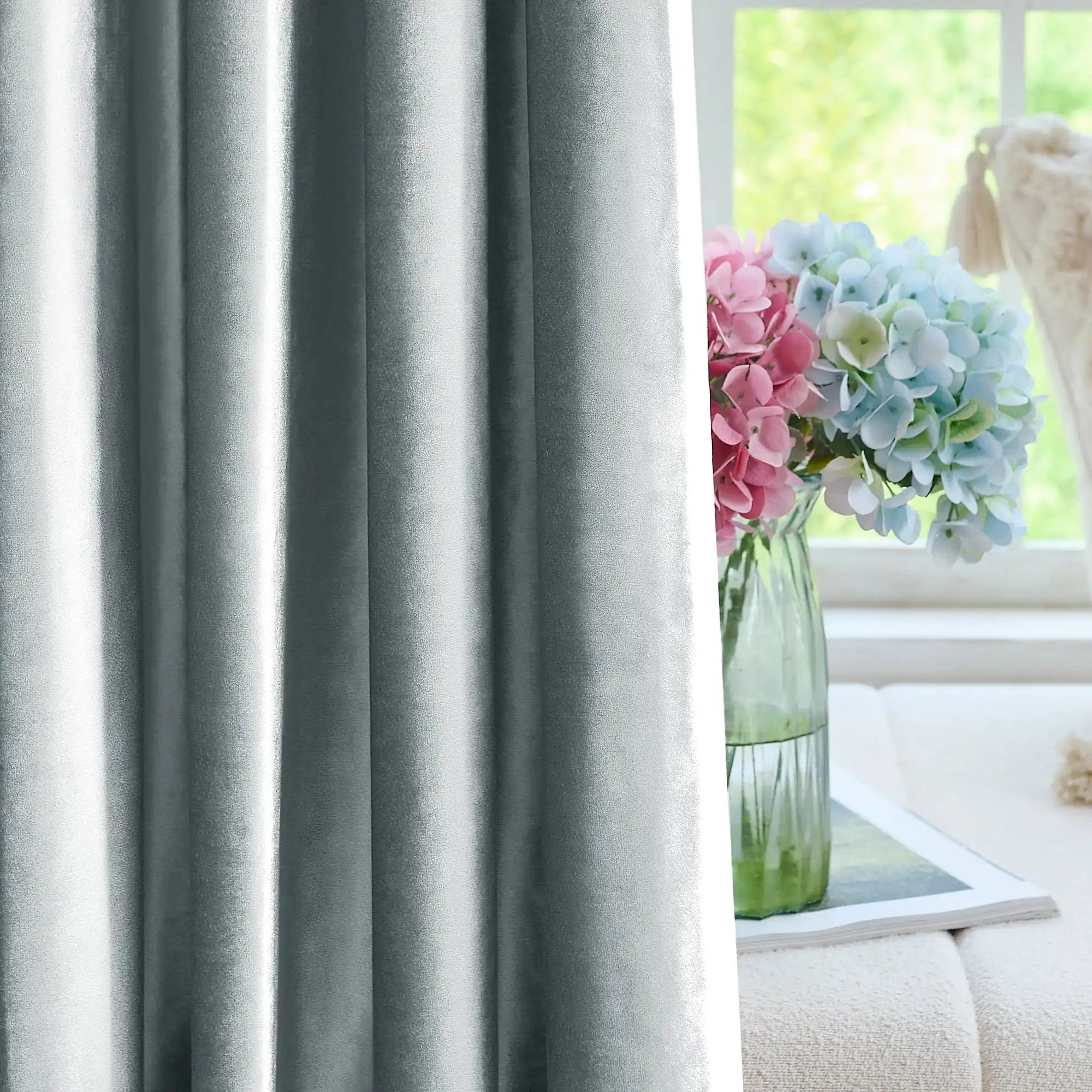 Luxurious gray velvet drapes with a subtle sheen, hanging on a black rod, in a stylish living space with decorative vases and flowers.