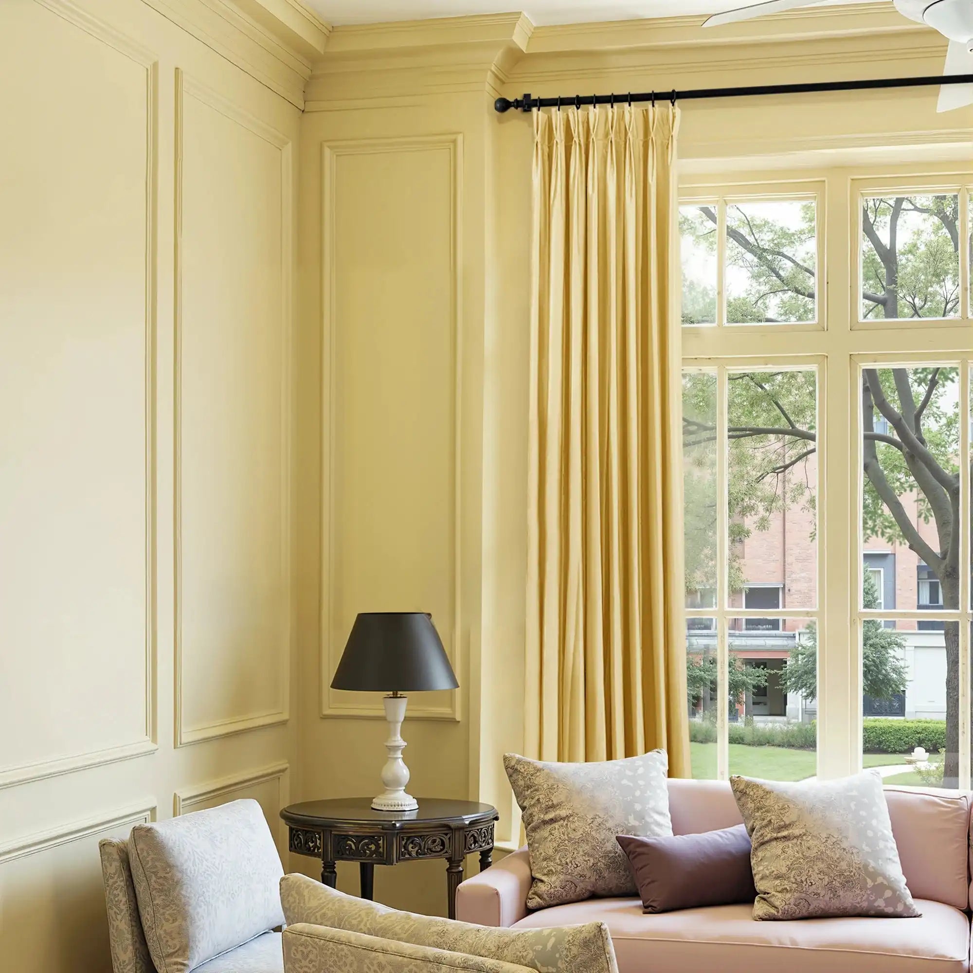 Close-up of yellow velvet curtain fabric with a smooth, luxurious texture, hanging in a well-lit room with large windows, elegant home decor