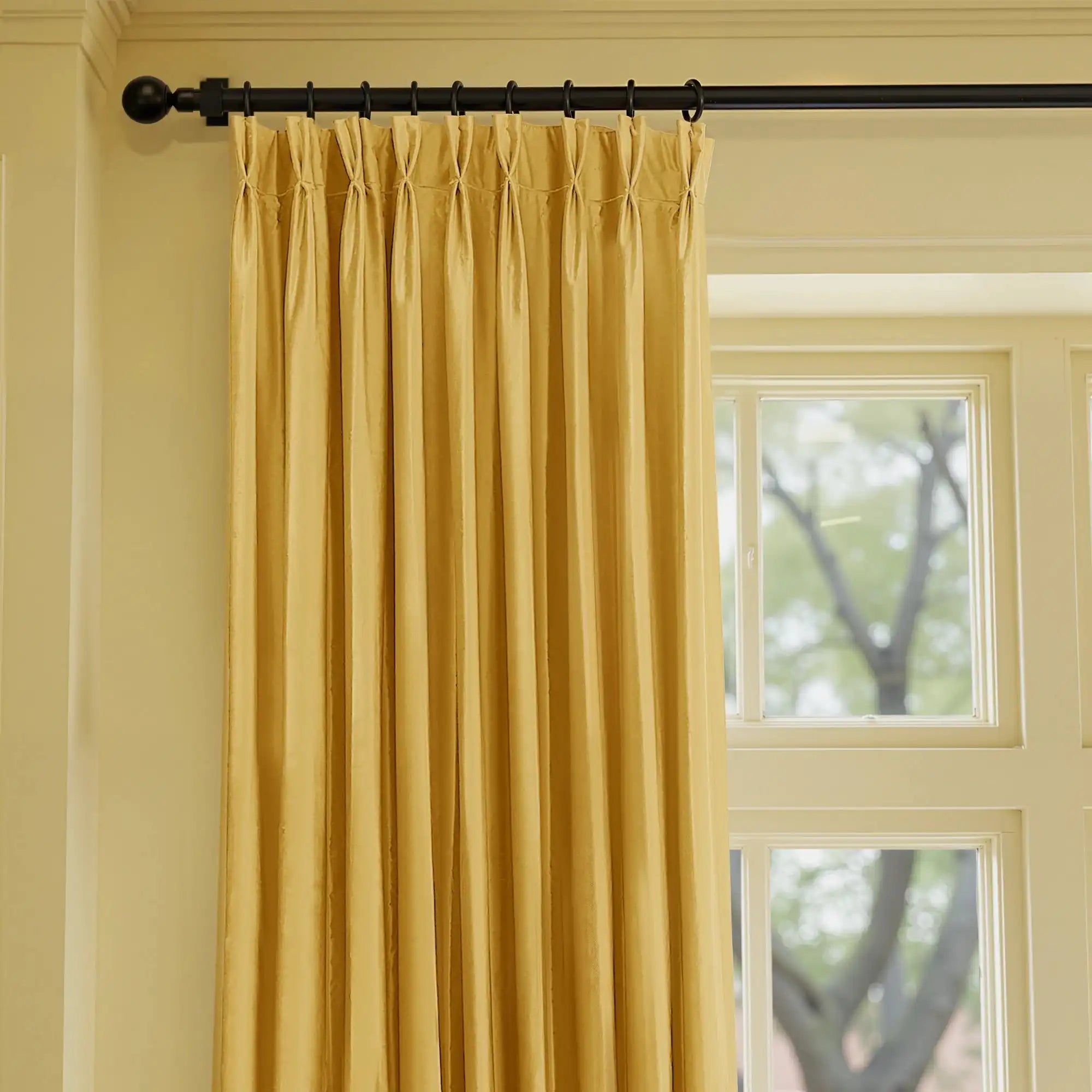 Yellow velvet curtains hanging on a black curtain rod in a bright room with large windows, soft fabric with a smooth texture, perfect for upscale interior decor