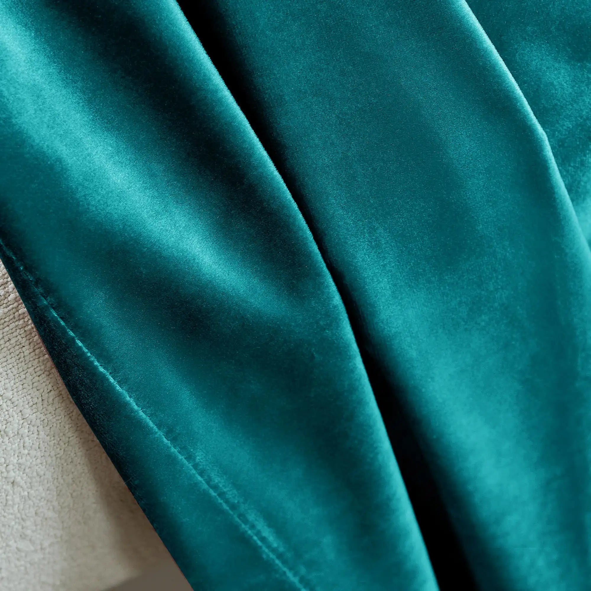 Close-up of teal velvet curtain fabric with soft texture and sheen, draped over curtain rod, luxurious home window treatment