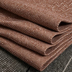 A macro photograph of the caramel fabric neatly folded into precise, crisp diagonal layers. The shot highlights the substantial weight and textured weave of the textile as it rests against a dark gray mottled surface.