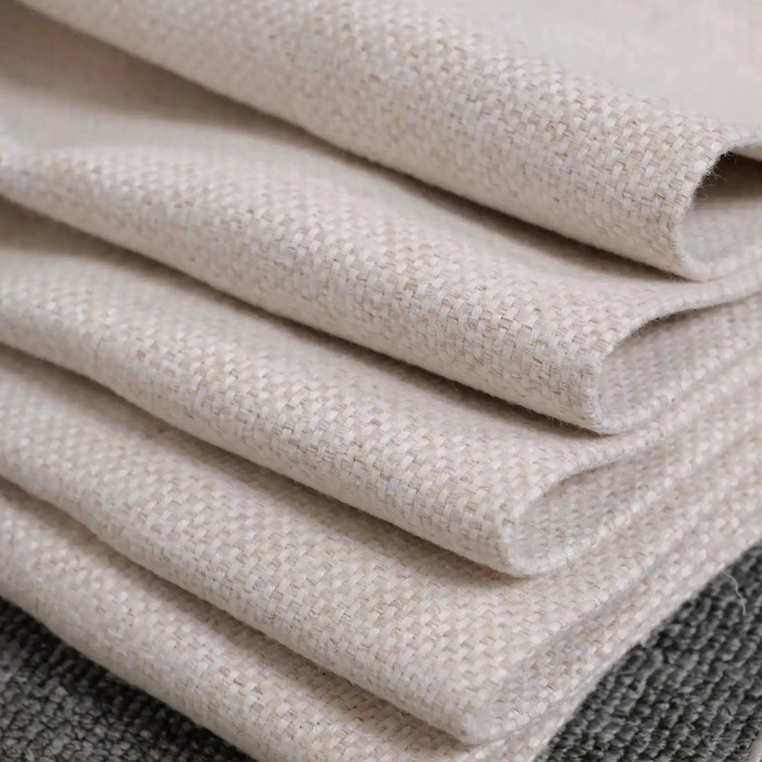 A close-up shot of the light yellow fabric neatly folded into multiple crisp layers, showcasing the texture of the textile weave resting against a dark gray background.
