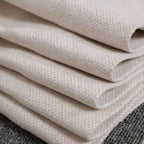 A close-up shot of the light yellow fabric neatly folded into multiple crisp layers, showcasing the texture of the textile weave resting against a dark gray background.