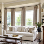 A full frontal view of the living room scene from a slightly lower angle, accentuating the elegant vertical lines of the grayish-brown curtains as they drape perfectly to the floor around the bay window.
