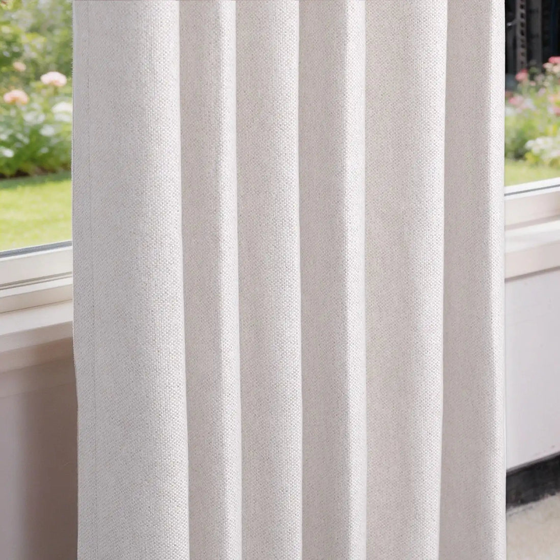 A crisp, close-up perspective of the hanging off-white curtain panel, highlighting its structured, uniform pleats and rich woven texture next to a window looking out onto a blurred garden view.