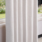 A crisp, close-up perspective of the hanging off-white curtain panel, highlighting its structured, uniform pleats and rich woven texture next to a window looking out onto a blurred garden view.
