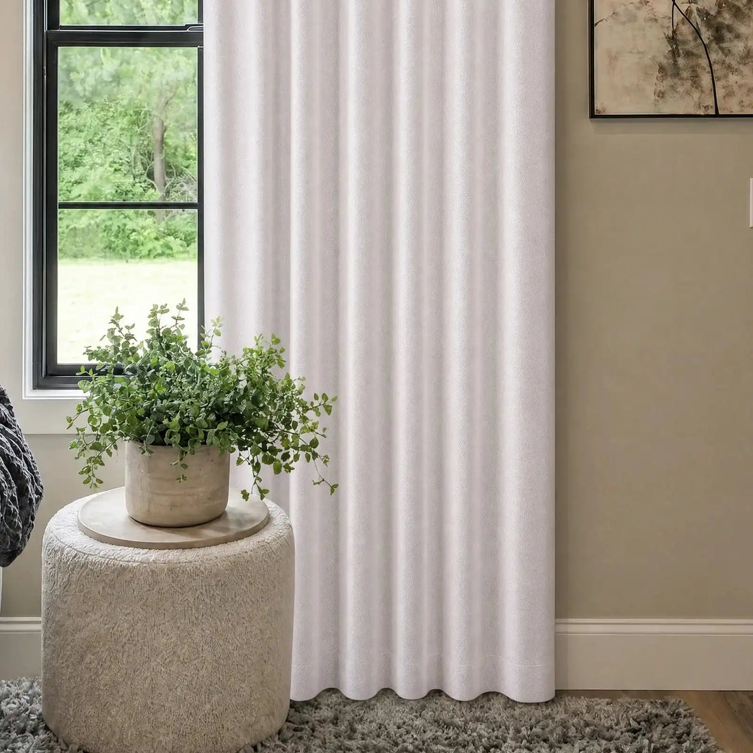 A medium shot focusing on the lower section of the off-white curtain panel, the white boucle ottoman with a green plant, and a soft gray knit blanket draped over the edge of the adjacent sofa.