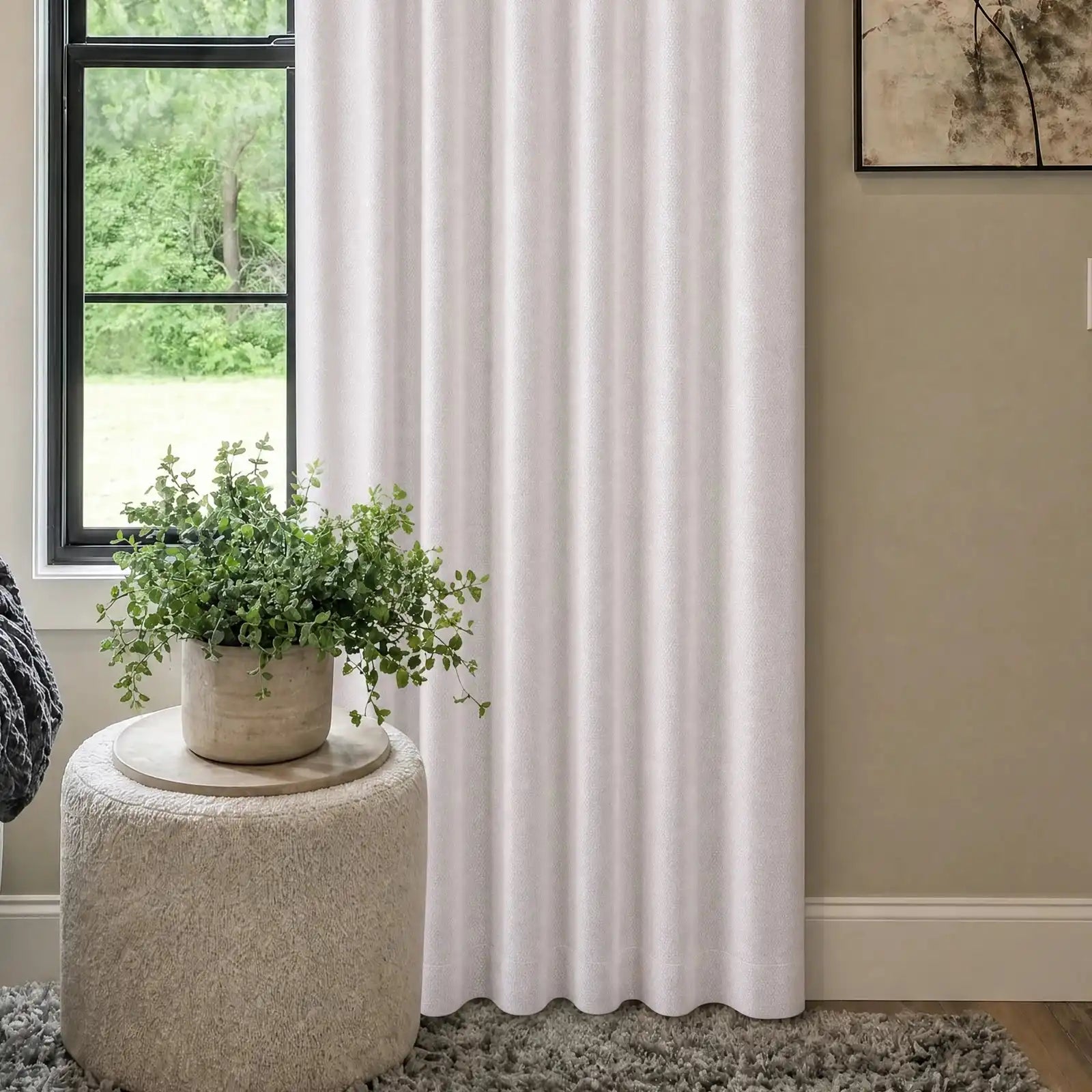 A medium shot focusing on the lower section of the off-white curtain panel, the white boucle ottoman with a green plant, and a soft gray knit blanket draped over the edge of the adjacent sofa.