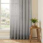 Beautifully draped Gray Sheila Cotton Semi Sheer Curtains next to a small wooden stool with a green plant