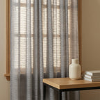 Soft textured Gray Sheila Cotton Semi Sheer Curtains against a wooden window frame in a cozy reading corner