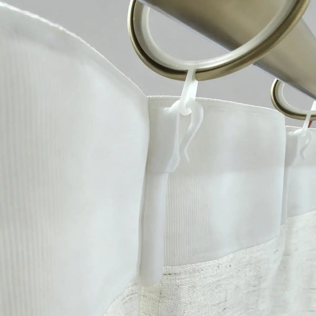 White curtain hooks made of high-polymer plastic securing white fabric curtains on metal rods, close-up view